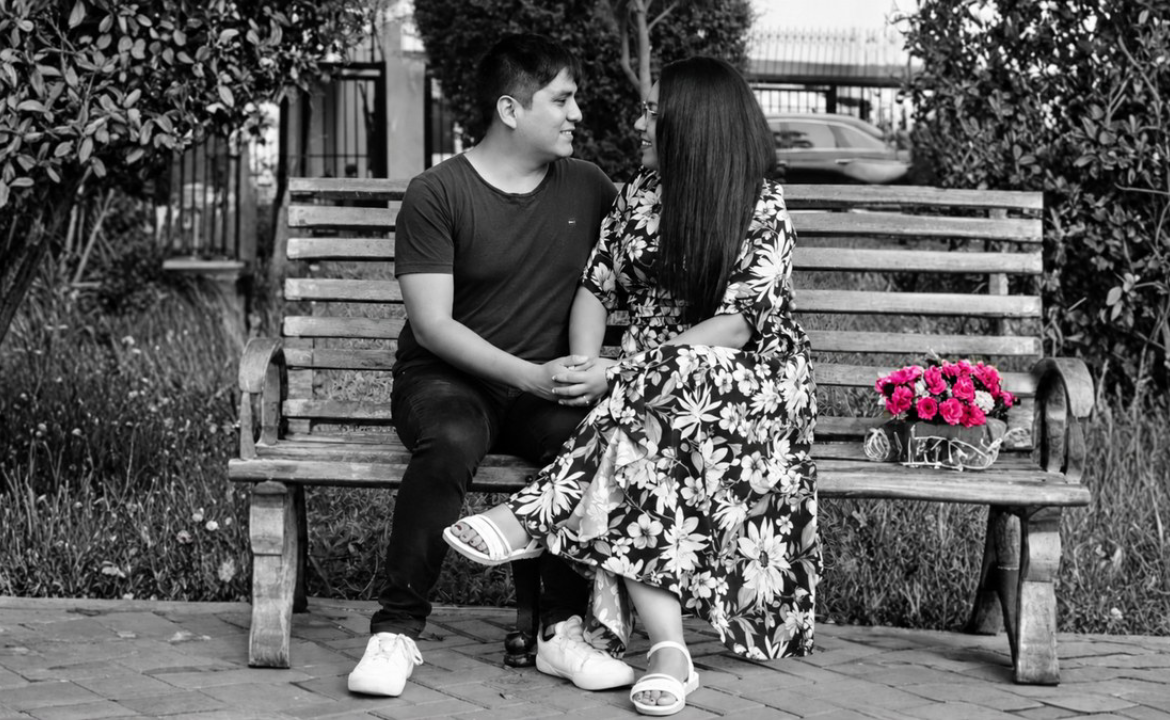 Nazarena and Robert sit on a bench, holding hands and looking at each other.